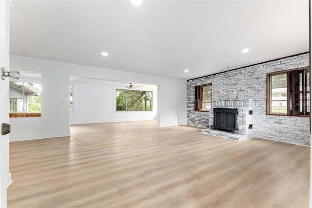 unfurnished living room featuring crown molding, a brick fireplace, and light wood-type flooring