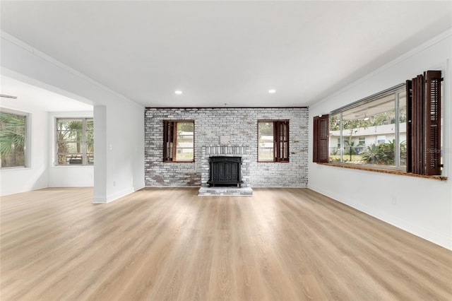 unfurnished living room with baseboards, a wealth of natural light, a brick fireplace, and light wood-style flooring