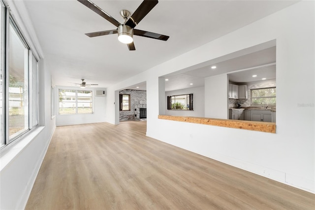 unfurnished living room with a healthy amount of sunlight, light wood finished floors, ceiling fan, and a large fireplace