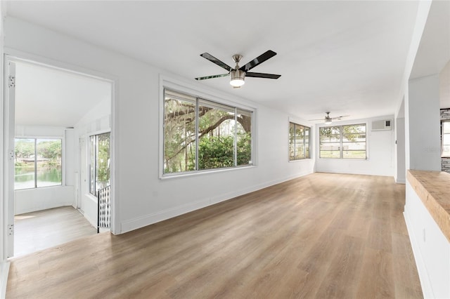 unfurnished living room with light wood-style flooring, a wall mounted air conditioner, a ceiling fan, and a healthy amount of sunlight
