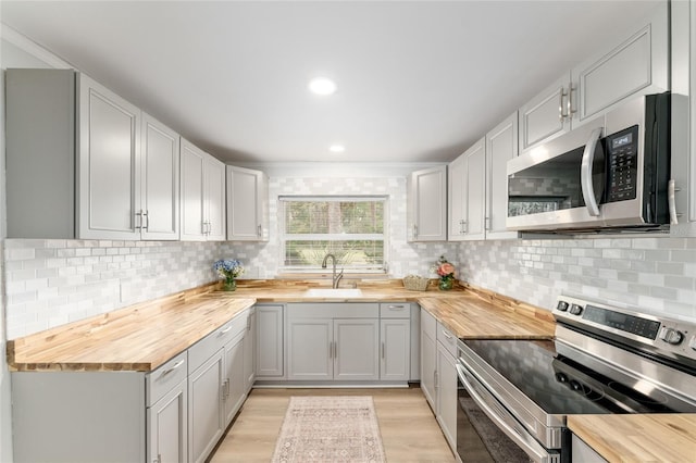 kitchen with light wood-style floors, butcher block countertops, appliances with stainless steel finishes, and a sink
