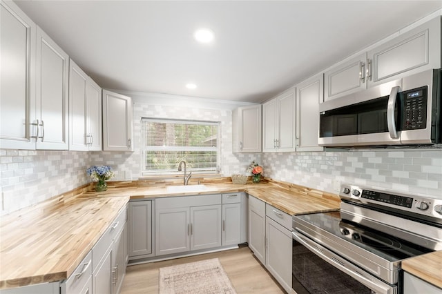 kitchen with wooden counters, a sink, light wood-style floors, tasteful backsplash, and appliances with stainless steel finishes