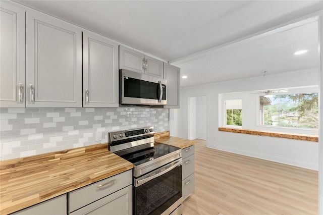 kitchen featuring butcher block countertops, light wood-style flooring, backsplash, and appliances with stainless steel finishes