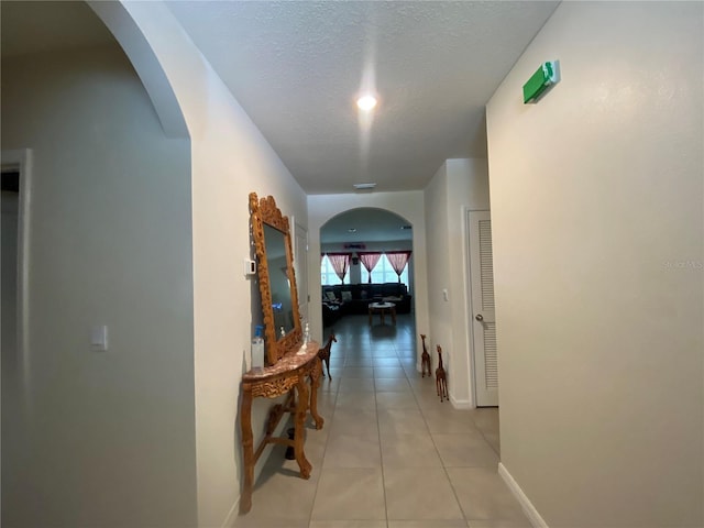 hall with arched walkways, light tile patterned floors, a textured ceiling, and baseboards