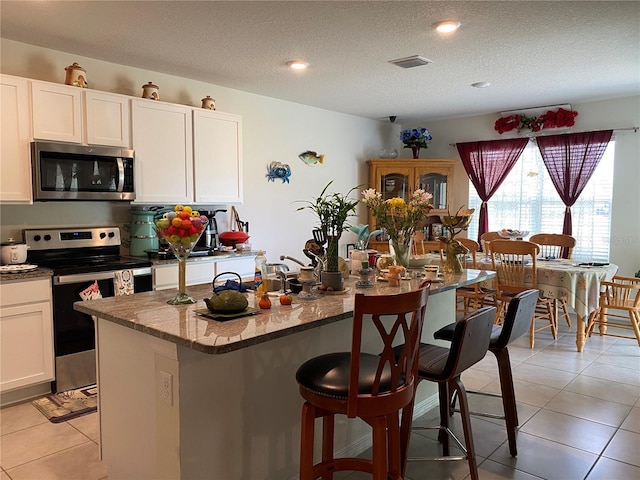 kitchen featuring appliances with stainless steel finishes, a breakfast bar, stone countertops, light tile patterned floors, and a center island