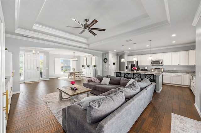 living area with a tray ceiling, dark wood-style floors, ornamental molding, a ceiling fan, and a chandelier