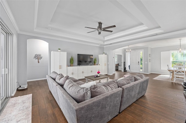 living room featuring arched walkways, a tray ceiling, ceiling fan, ornamental molding, and baseboards
