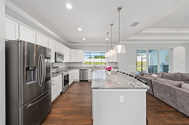 kitchen with appliances with stainless steel finishes, open floor plan, dark wood-type flooring, a kitchen island, and crown molding