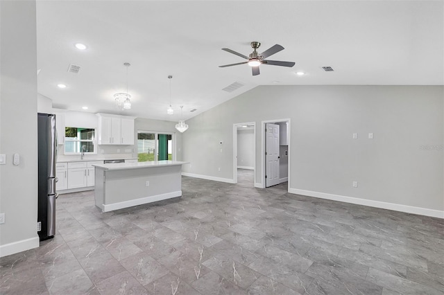 interior space featuring freestanding refrigerator, lofted ceiling, a center island, open floor plan, and light countertops