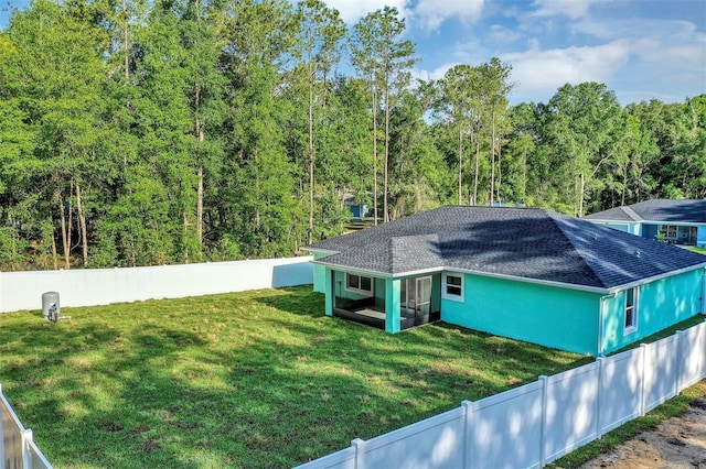 view of side of property featuring a fenced backyard, a shingled roof, a forest view, and a yard