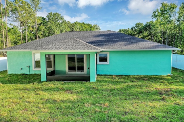 rear view of house with a yard, stucco siding, roof with shingles, and fence