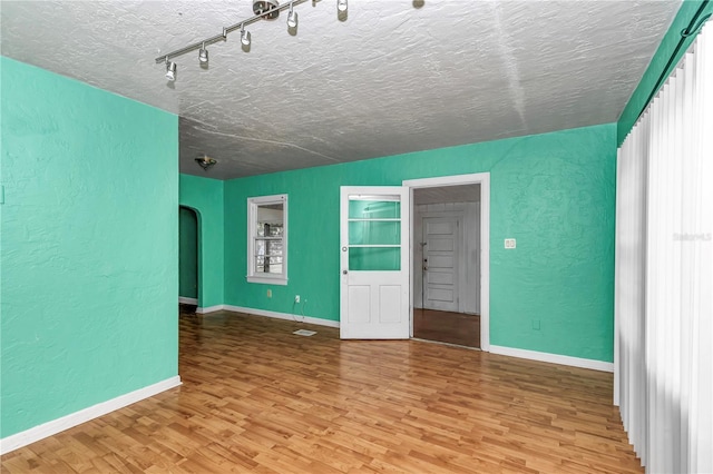 spare room featuring a textured wall, wood finished floors, a textured ceiling, baseboards, and arched walkways