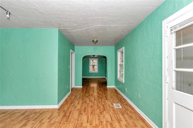 corridor with wood finished floors, a textured wall, a textured ceiling, arched walkways, and baseboards