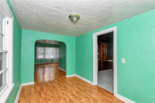 empty room featuring arched walkways, wood finished floors, a textured ceiling, baseboards, and a textured wall