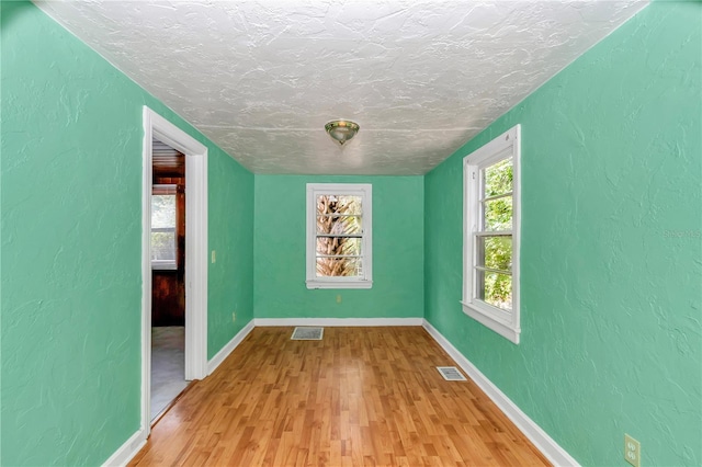empty room with light wood-style floors, a textured ceiling, baseboards, and a textured wall
