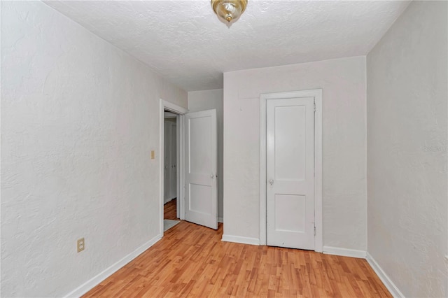 unfurnished bedroom featuring light wood-style floors, baseboards, a textured ceiling, and a textured wall