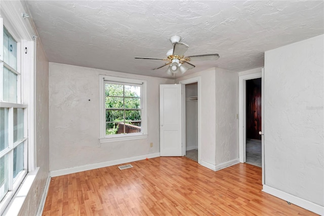 unfurnished bedroom with light wood-type flooring, baseboards, a textured ceiling, a ceiling fan, and a textured wall