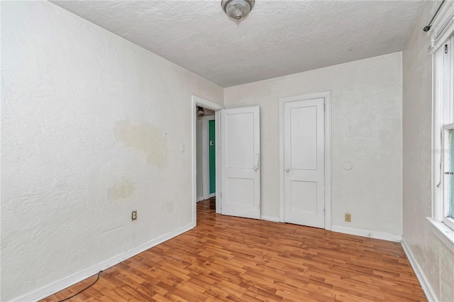 unfurnished bedroom with light wood finished floors, baseboards, a textured ceiling, and a textured wall