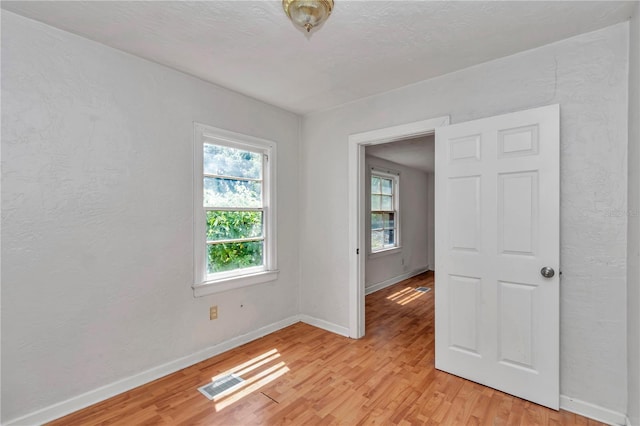 empty room with light wood finished floors, baseboards, and a textured wall