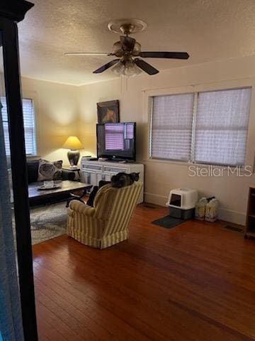 living area featuring wood finished floors, a ceiling fan, baseboards, and a textured ceiling