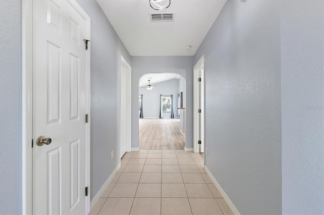 corridor featuring arched walkways, light tile patterned flooring, baseboards, and a textured wall
