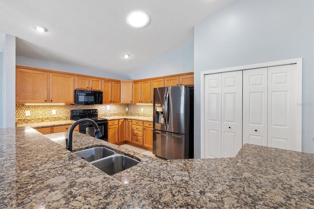 kitchen featuring black appliances, a sink, backsplash, vaulted ceiling, and dark stone countertops
