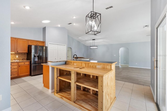 kitchen with stainless steel refrigerator with ice dispenser, arched walkways, lofted ceiling, light tile patterned floors, and backsplash