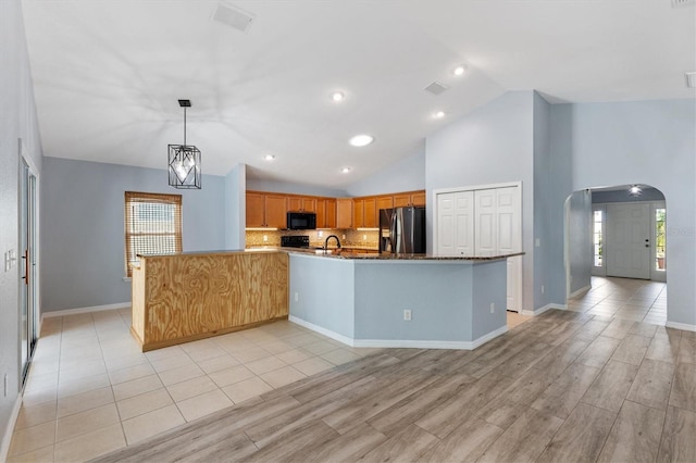 kitchen with black appliances, decorative backsplash, light wood finished floors, decorative light fixtures, and a large island
