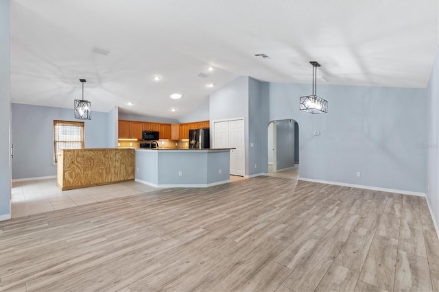 unfurnished living room featuring vaulted ceiling, arched walkways, light wood-style floors, and baseboards