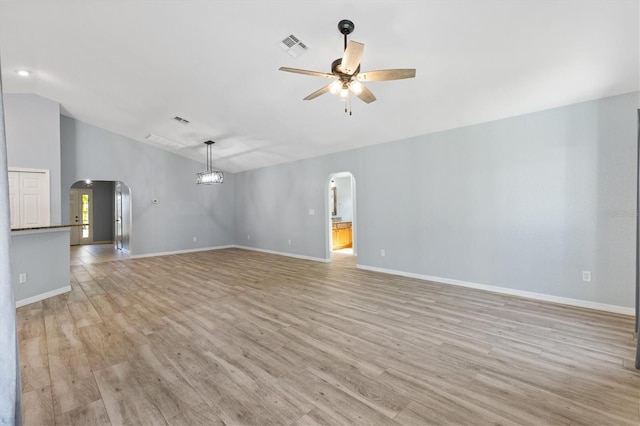unfurnished living room with arched walkways, ceiling fan, vaulted ceiling, light wood-style floors, and baseboards
