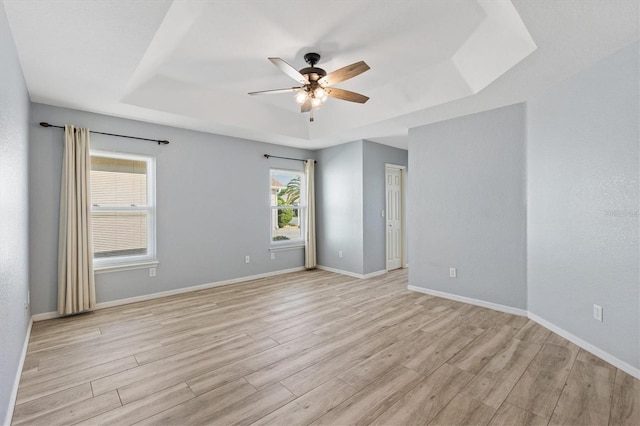 empty room featuring a raised ceiling, a ceiling fan, light wood-style floors, and baseboards