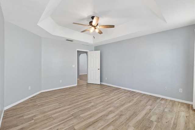 unfurnished room featuring a raised ceiling, ceiling fan, light wood-style floors, and baseboards