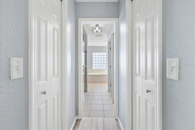 corridor with a textured wall and light wood finished floors