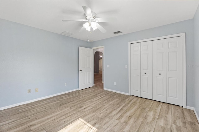 unfurnished bedroom featuring baseboards, light wood-style floors, arched walkways, and a closet
