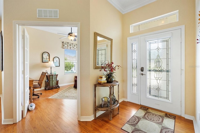 foyer with ornamental molding, wood finished floors, a ceiling fan, baseboards, and a towering ceiling