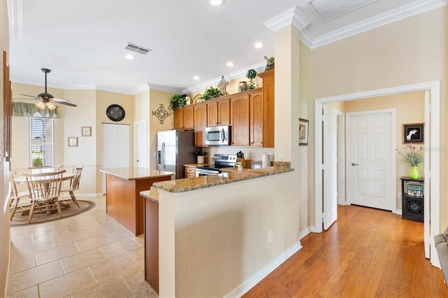 kitchen featuring stainless steel appliances, a center island, brown cabinetry, light stone countertops, and ornamental molding