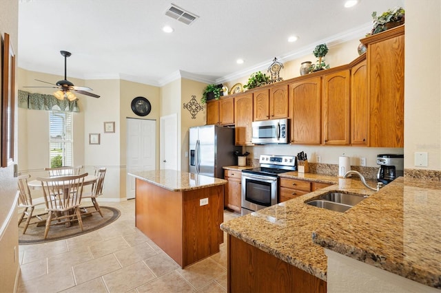 kitchen featuring stainless steel appliances, a sink, a kitchen island, brown cabinetry, and light stone countertops