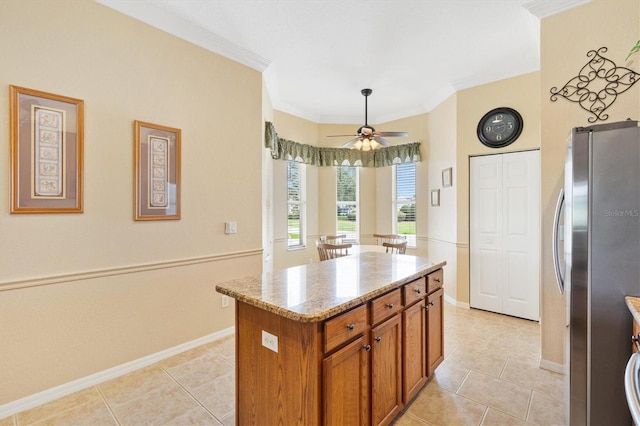 kitchen featuring freestanding refrigerator, brown cabinets, light tile patterned flooring, baseboards, and a center island