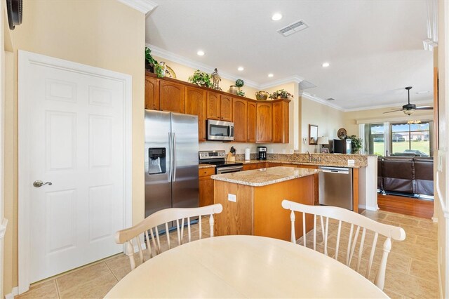 kitchen featuring appliances with stainless steel finishes, a kitchen island, crown molding, a peninsula, and light tile patterned flooring