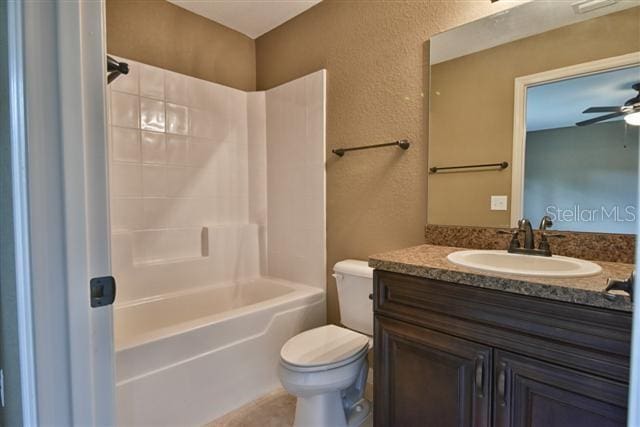 full bath featuring toilet, ceiling fan, vanity, tub / shower combination, and a textured wall