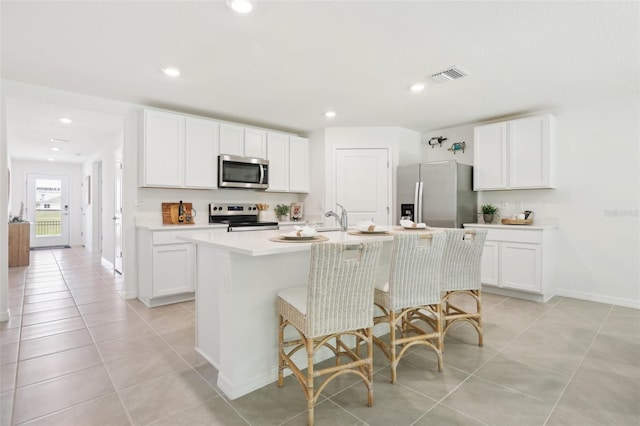 kitchen with visible vents, an island with sink, light countertops, light tile patterned floors, and appliances with stainless steel finishes