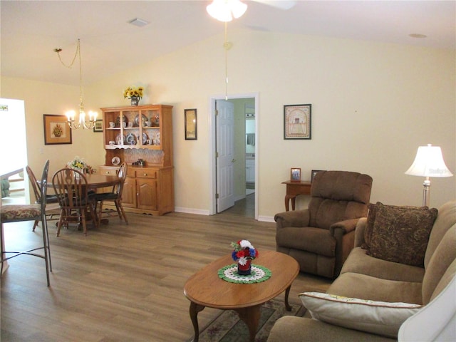 living room featuring baseboards, visible vents, ceiling fan with notable chandelier, vaulted ceiling, and wood finished floors