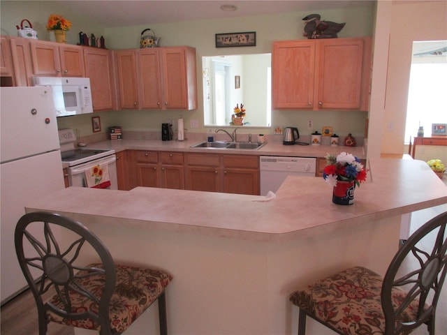 kitchen with light brown cabinetry, a breakfast bar, white appliances, a sink, and light countertops