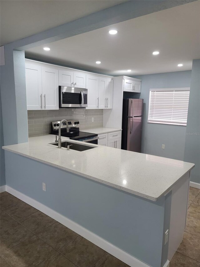 kitchen with appliances with stainless steel finishes, a sink, a peninsula, light stone counters, and recessed lighting
