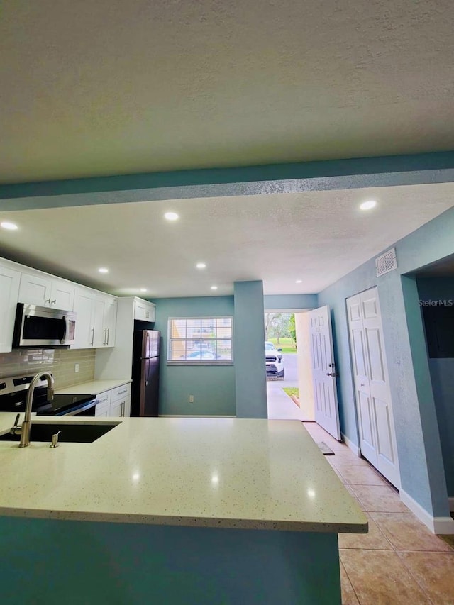 kitchen featuring stainless steel appliances, light stone counters, white cabinetry, a sink, and decorative backsplash