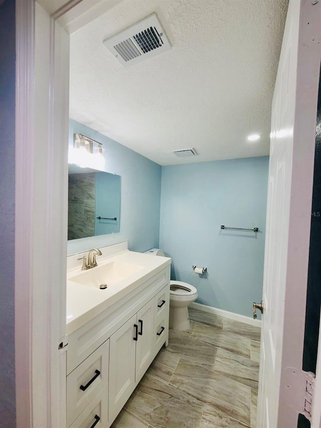 bathroom with vanity, toilet, a textured ceiling, and baseboards