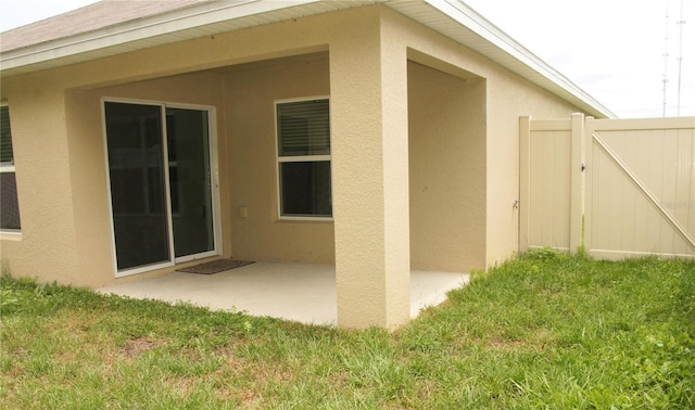 view of side of property featuring stucco siding, a patio area, a gate, and a yard