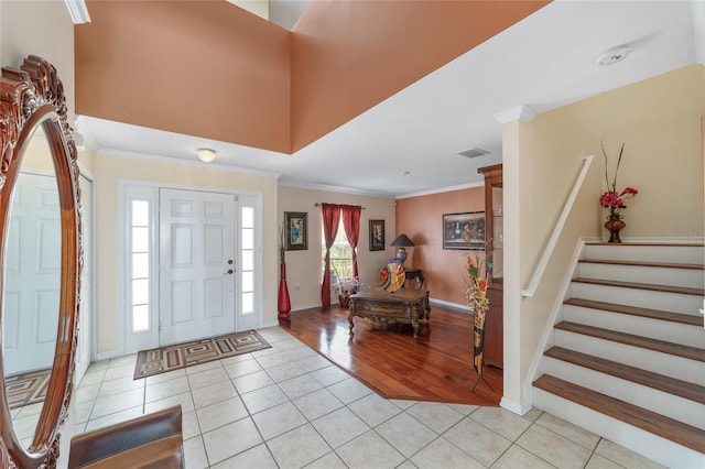 entrance foyer featuring light tile patterned floors, crown molding, baseboards, and stairs