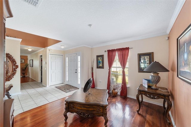 foyer featuring crown molding, light wood-style floors, baseboards, and a textured ceiling