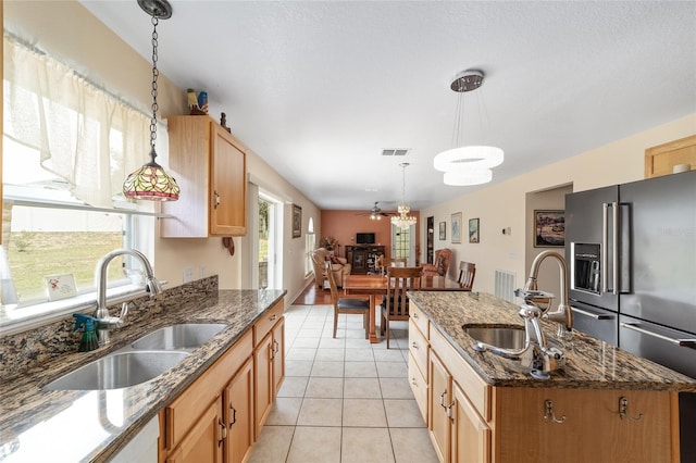 kitchen with a sink, high end refrigerator, an island with sink, pendant lighting, and light tile patterned floors
